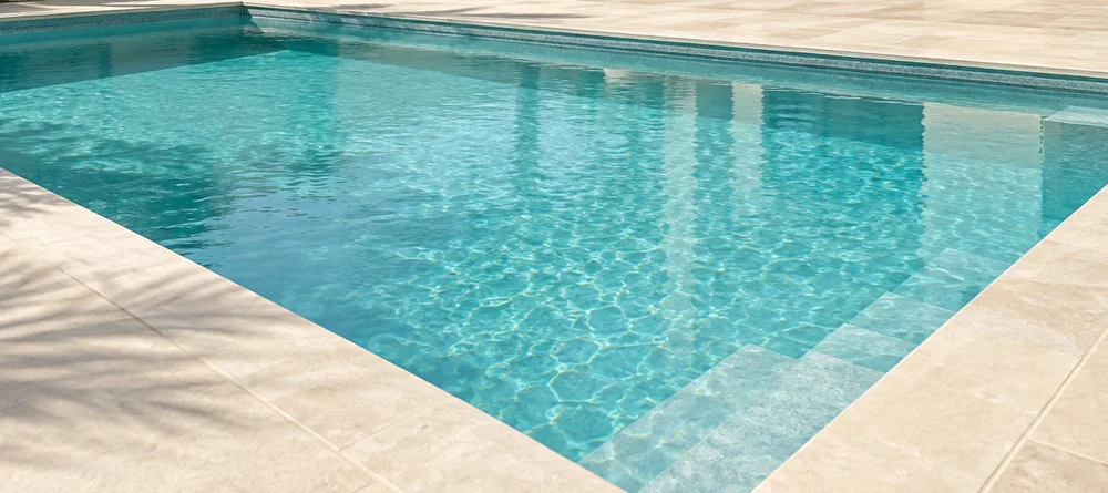 Sunlight on clear turquoise pool water and a pale stone pool edge